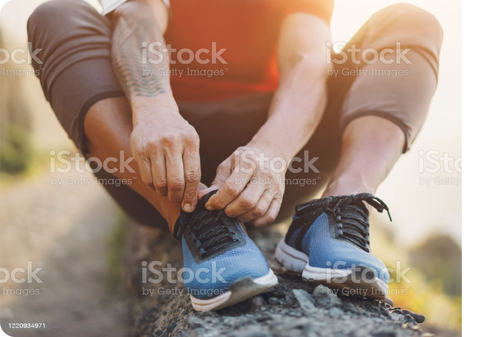 A person sitting on a fallen tree outside, wearing athletic clothes, and tying their shoes.