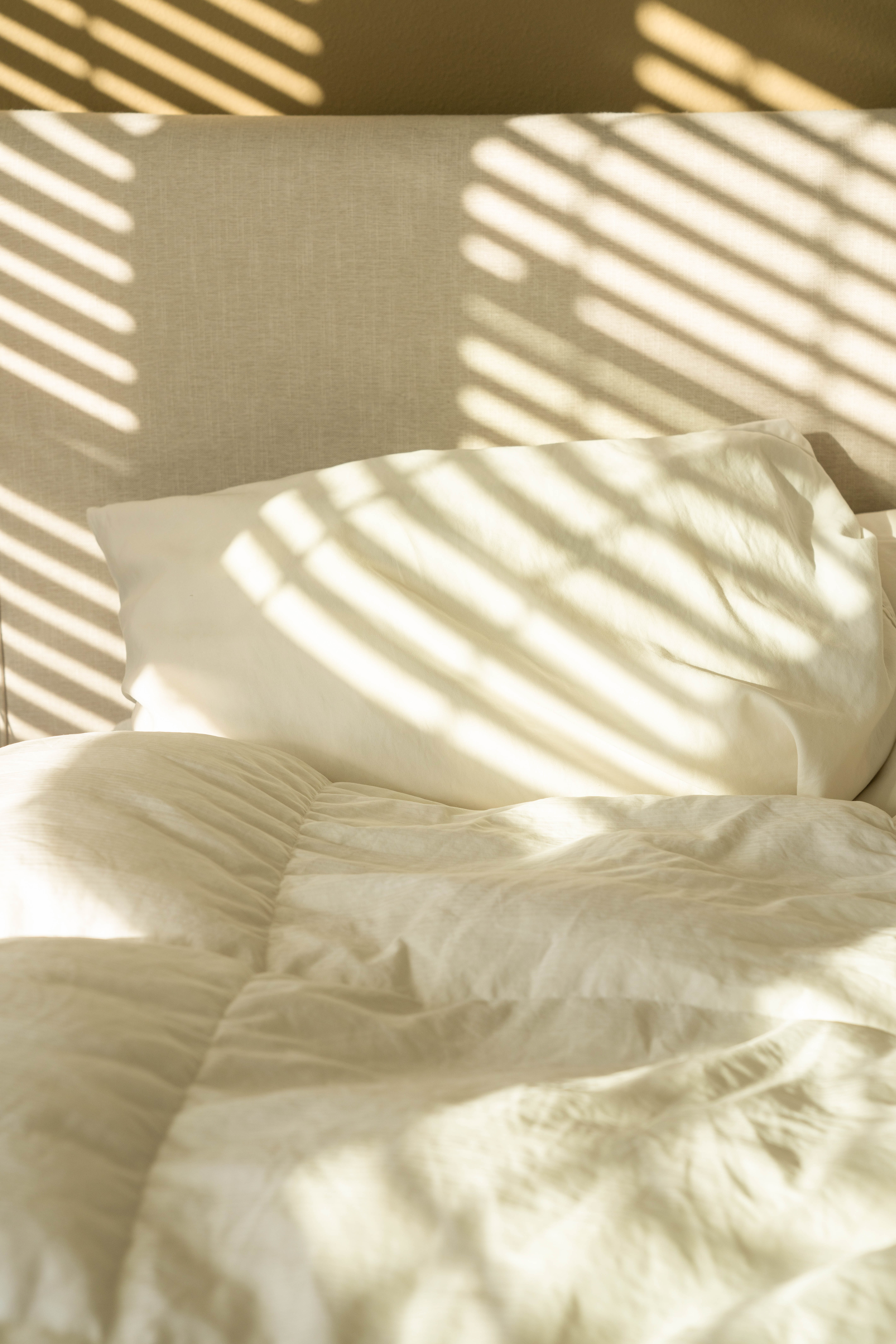 An empty bed decorated by light streaming through a window.