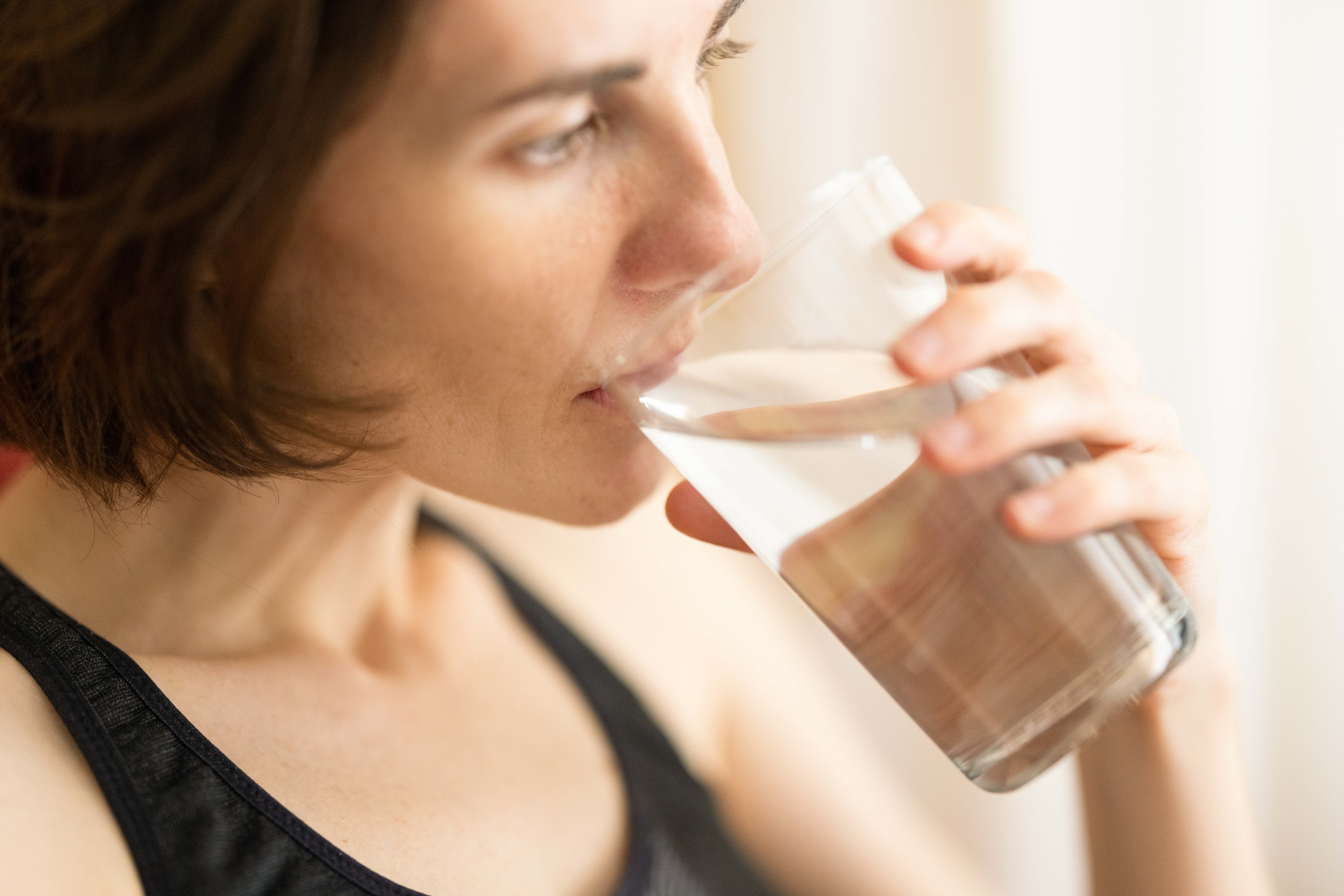 A person drinking a glass of water. They have light skin and brown hair and are looking peacefully out a window.